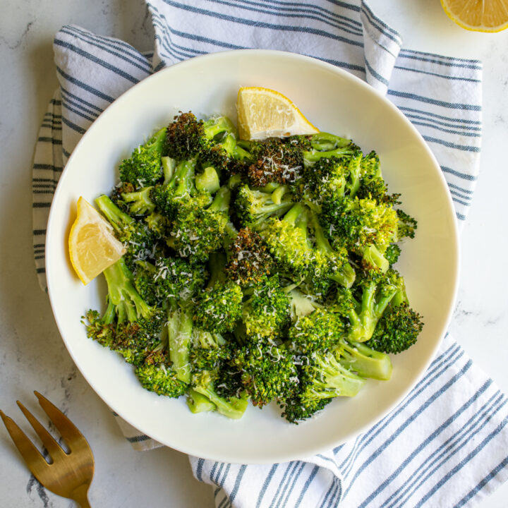 A white bowl on a blue stripped towel filled with air fryer broccoli and garnished with melon wedges.