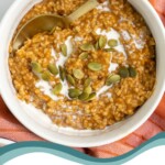 Pinterest Pin with text 'Instant Pot Pumpkin Steel Cut Oats', image of a white bowl with pumpkin oatmeal and garnished with cream and pumpkin seeds.