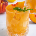 Pinterest pin with text over lay 'Peach Bourbon Smash', image of a glass filled with a peach bourbon cocktail garnished with a peach slice and fresh basil leaves.