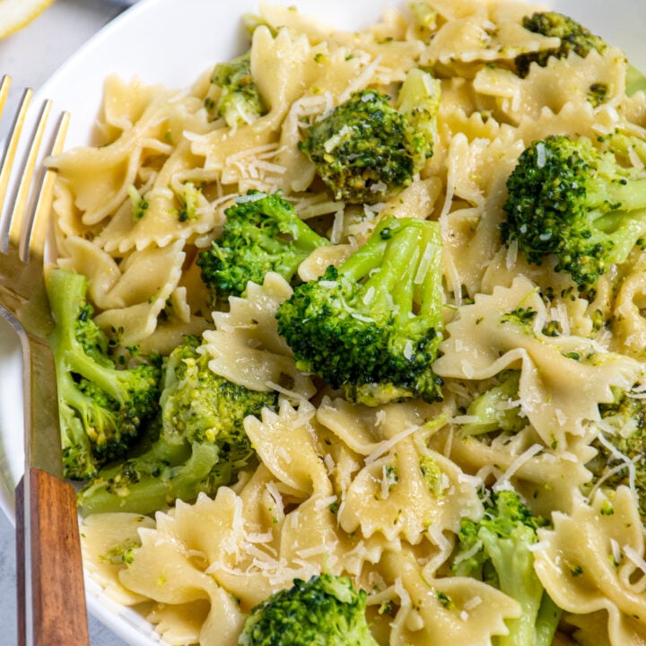 Close up of bowties and broccoli in a white bowl with a fork.