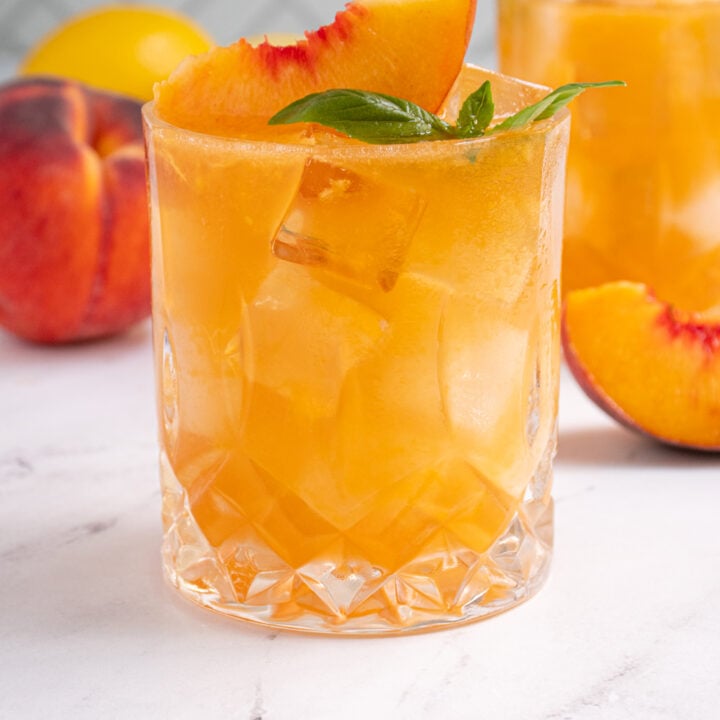 Glass with a Bourbon Peach Smash with a peach slice and fresh basil leaves to garnish the glass.
