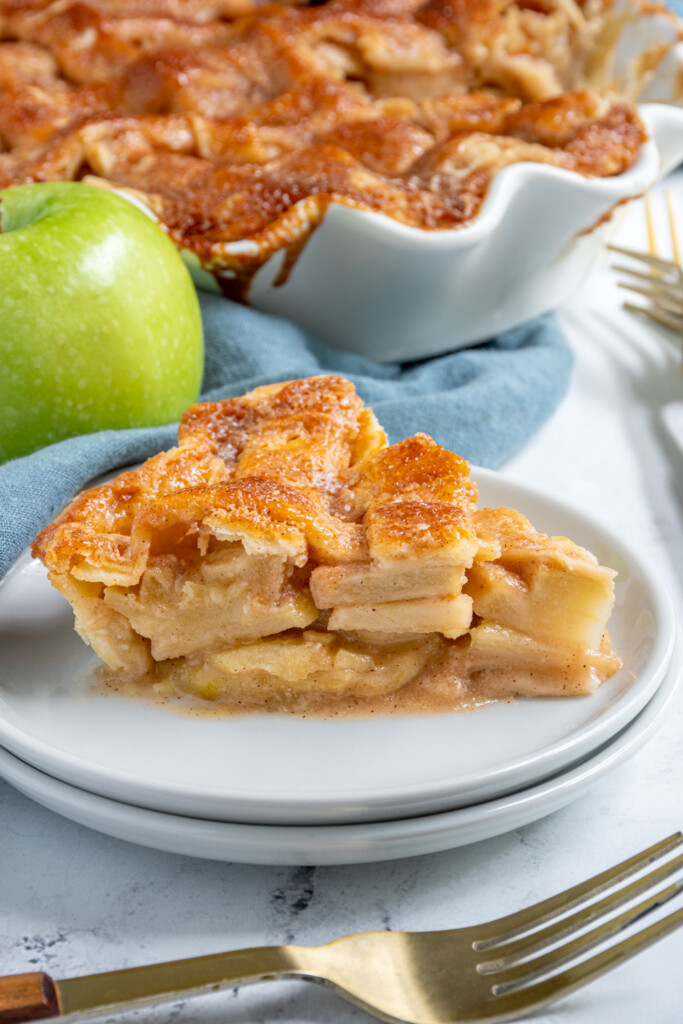 A close up of an apple pie slice on a plate showing off the apples inside.