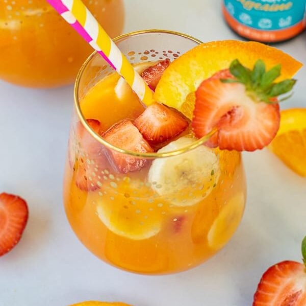 fresh colorful fruit in a glass of orange juice with a paper straw