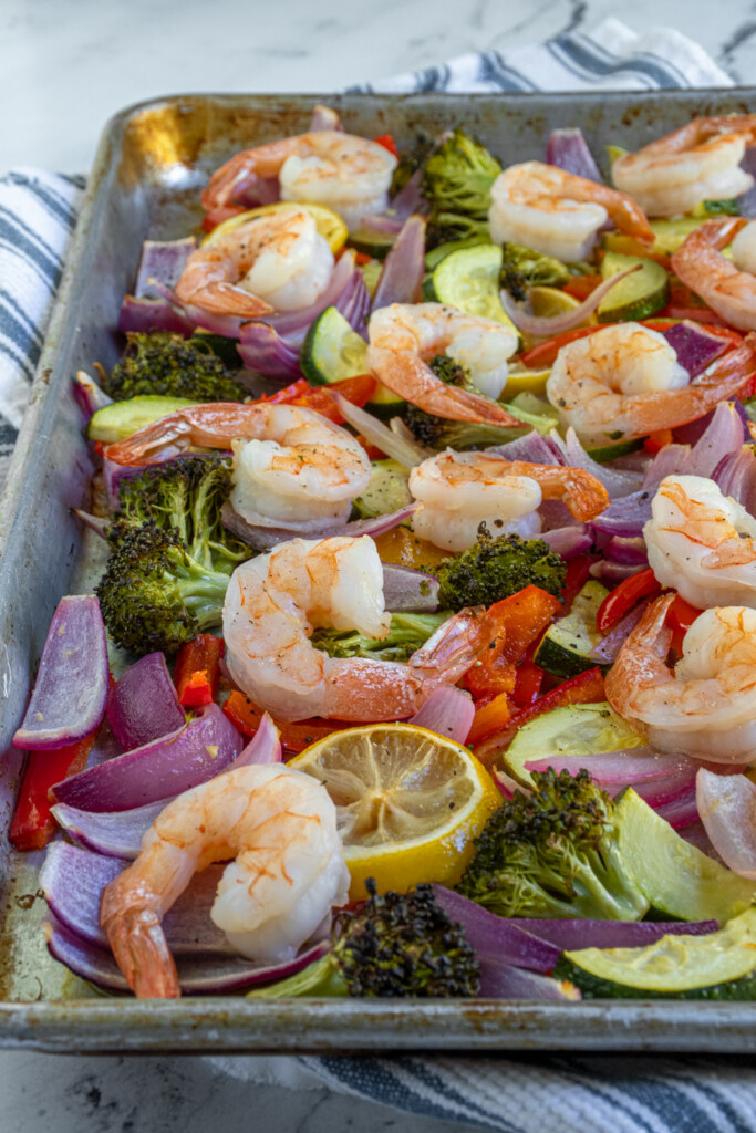Side view of a sheet pan filled with shrimp and veggies.