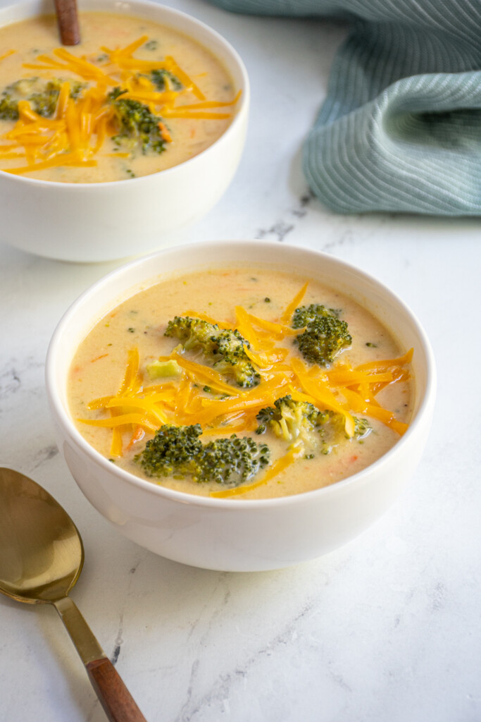 Two bowls on a table filled with healthy broccoli cheese soup garnished with extra cheddar cheese.