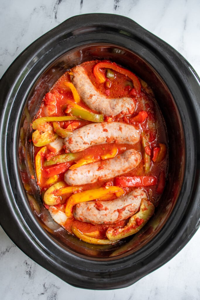 Overhead view of freshly cooked Italian sausages in the crockpot with sliced bell peppers and onions.