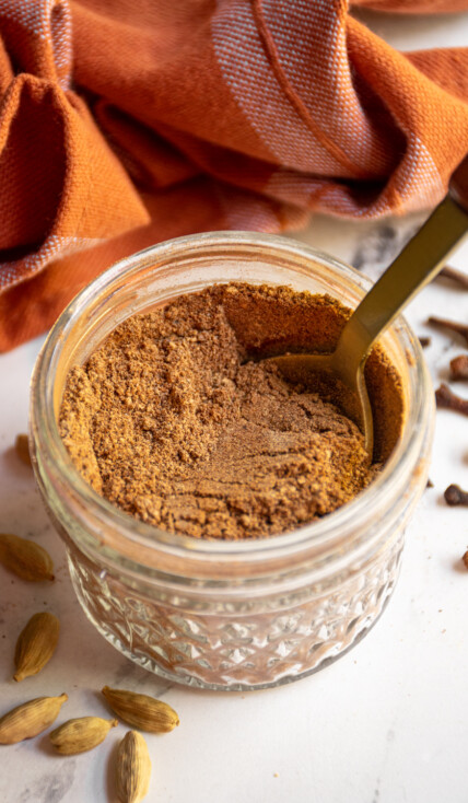 Small jar filled with chai spice blend and a gold spoon.