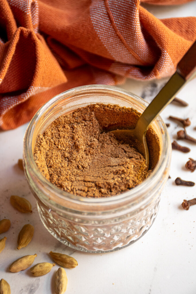 Small jar filled with chai spice blend and a gold spoon.
