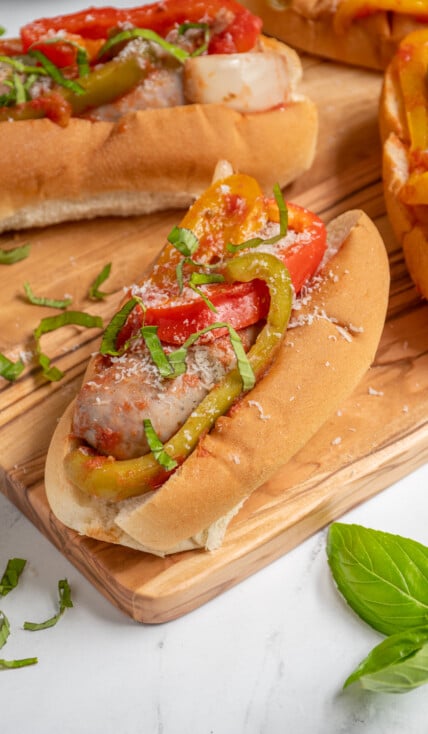 An Italian Sausage with peppers and onions in a bun topped with fresh basil and grated parmesan cheese.