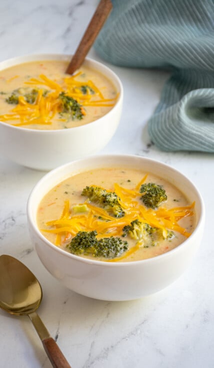 White bowls filled with healthy broccoli cheese soup topped with extra cheddar cheese.