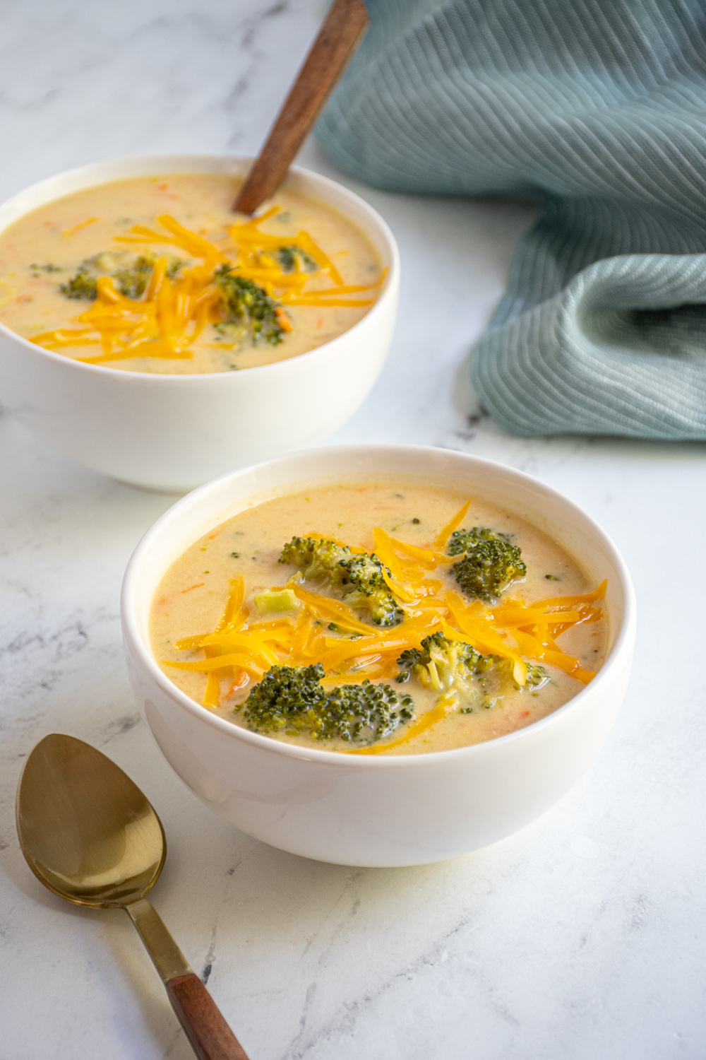White bowls filled with healthy broccoli cheese soup topped with extra cheddar cheese.
