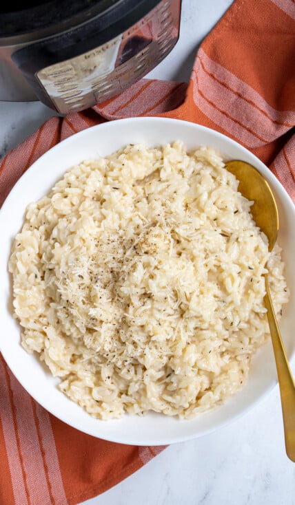 Overhead view of Instant Pot Risotto in a large white bowl with a gold serving spoon topped with fresh parmesan and black pepper.
