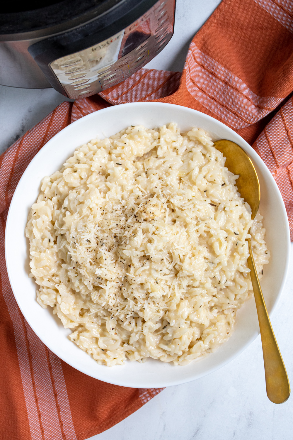 Overhead view of Instant Pot Risotto in a large white bowl with a gold serving spoon topped with fresh parmesan and black pepper.