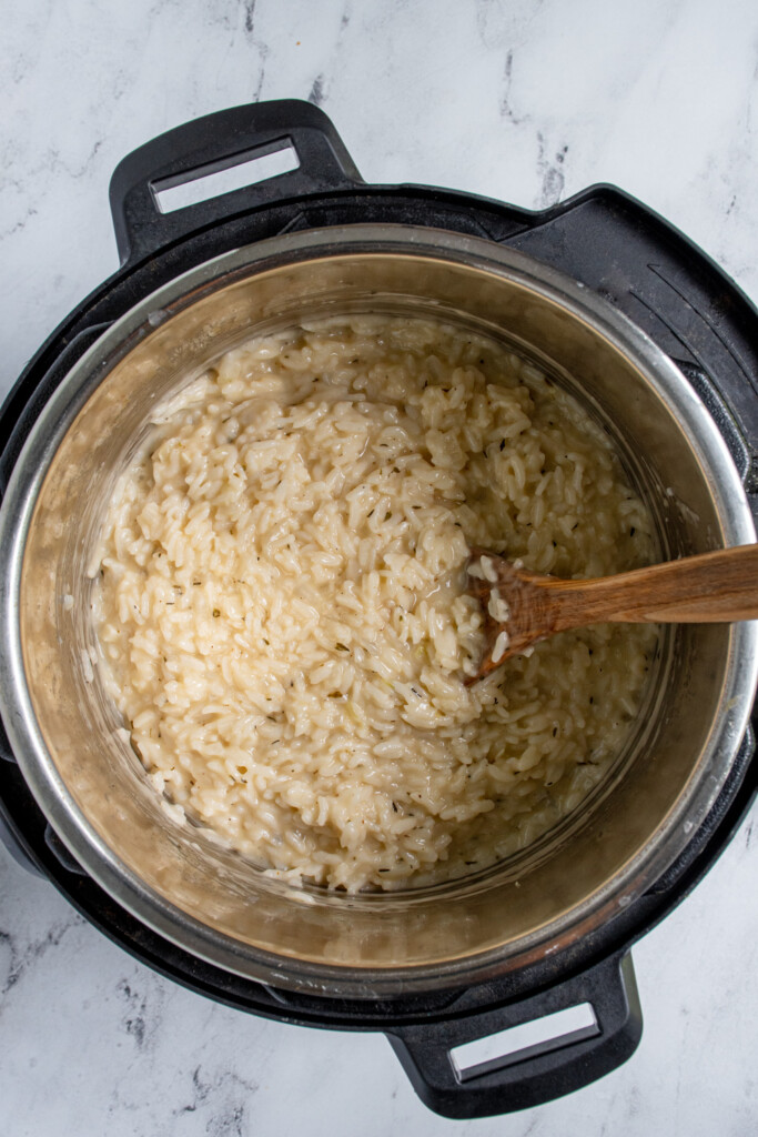 Overhead view of a pressure cooker with freshly made risotto inside with a wooden spoon.