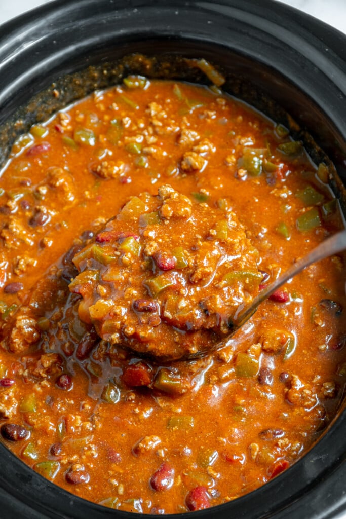 A ladle in a crockpot full of the best classic chili with ground beef, bean, and peppers.
