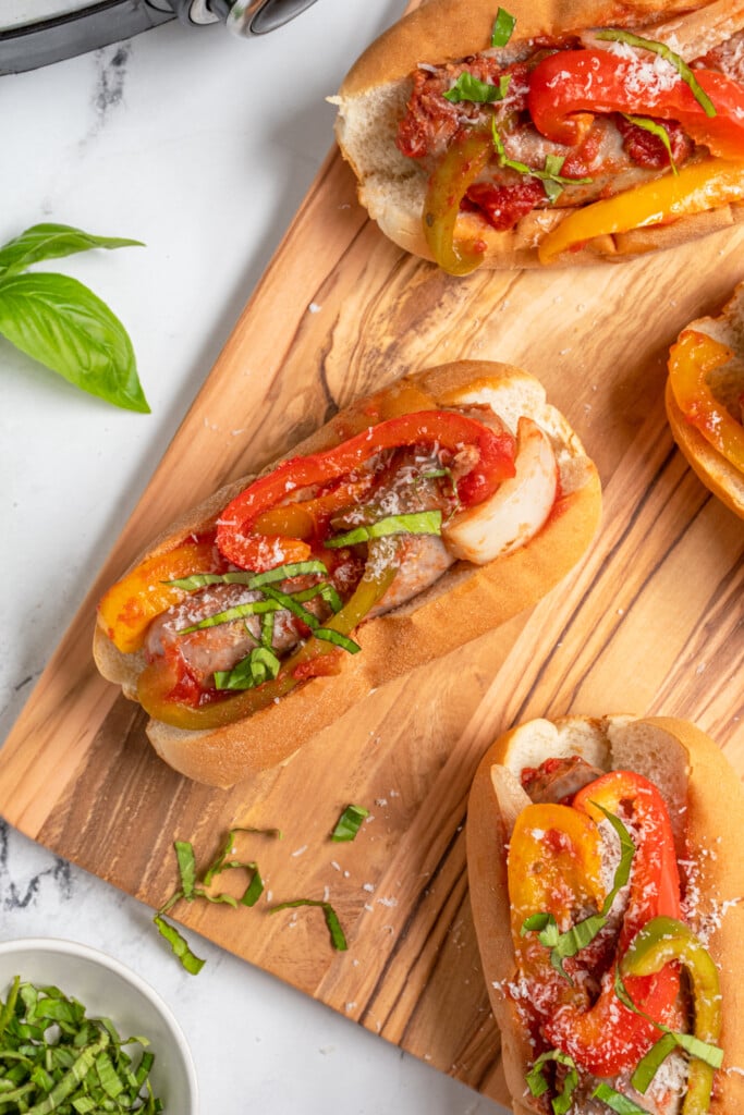 Overhead view of an Italian sausage in a bun with peppers and topped with basil and parmesan cheese.