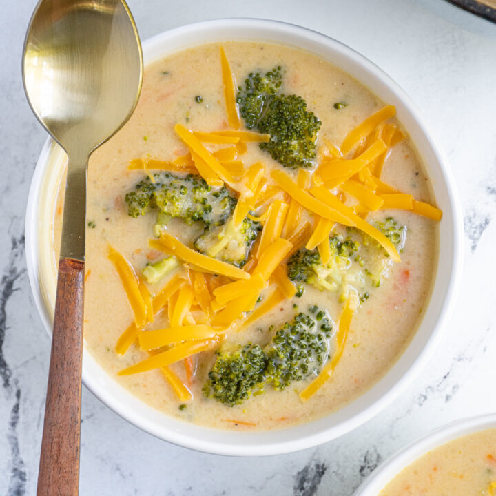 Overhead view of a white bowl filled with fresh broccoli cheddar soup topped with extra cheddar cheese.