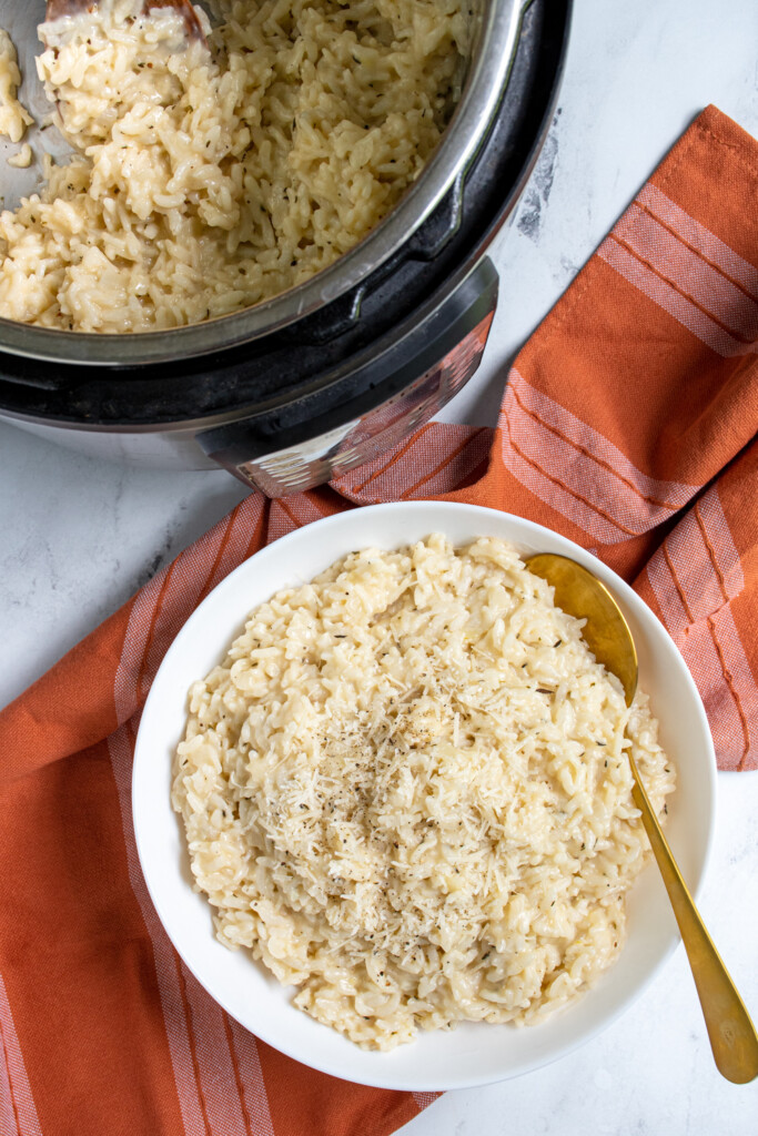 Overhead view of a large white bowl filled with instant pot risotto with fresh parmesan on top and a serving spoon.