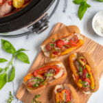 Pinterest Pin with logo 'The Schmidty Wife', image of Italian sausages in bun with peppers next to a crockpot.