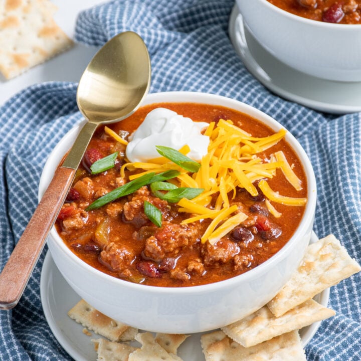Bowl of classic crockpot chili with ground beef, beans, and peppers topped with garnishes and a spoon for eating.