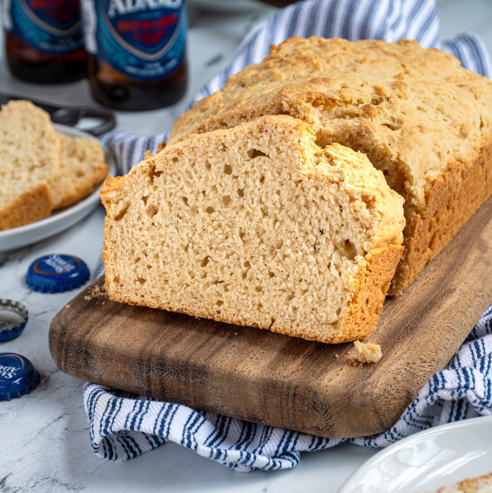 A slice of beer bread on a cutting board propped up against a loaf of easy beer bread.