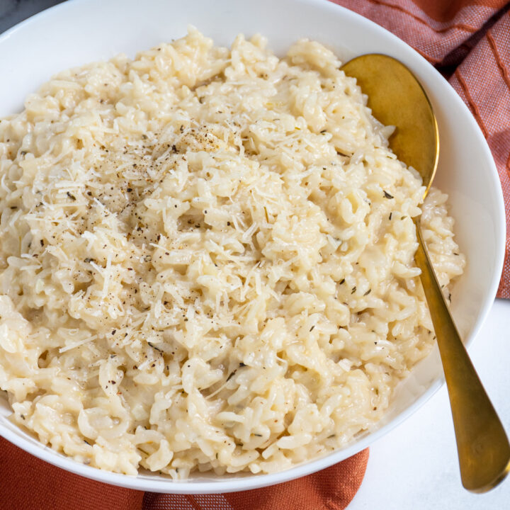 A serving bowl filled with risotto made in the pressure cooker with a serving spoon.