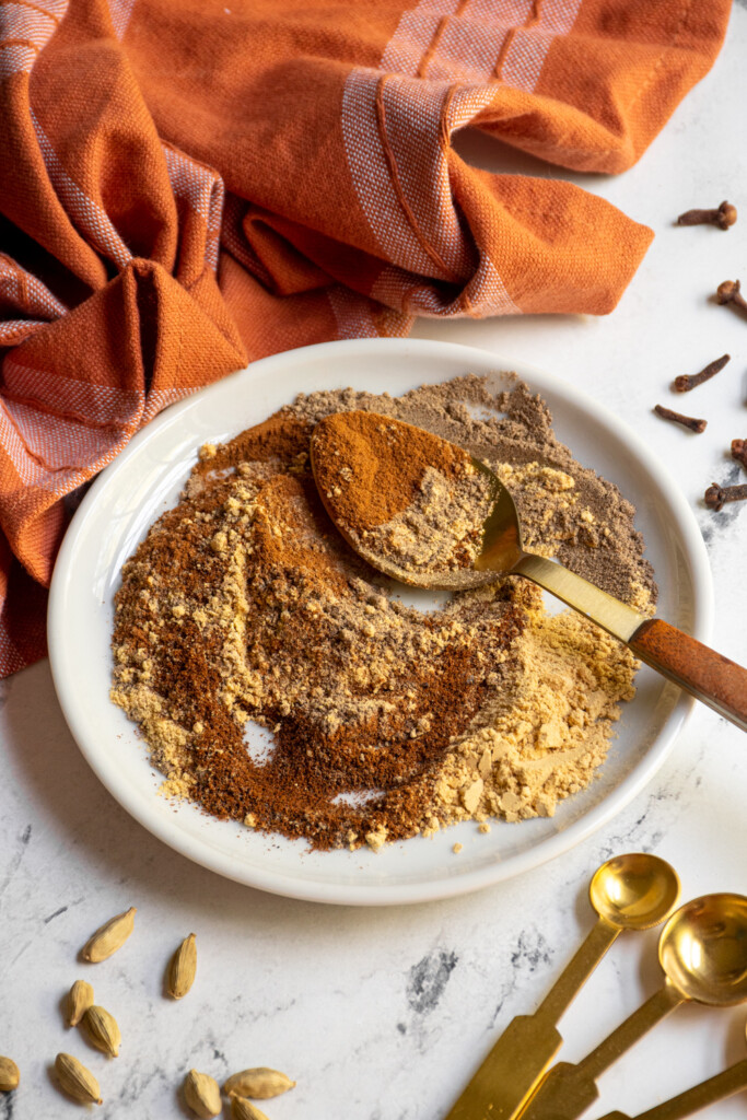 Small white plate with a gold spoon stirring together the spices that make up chai.