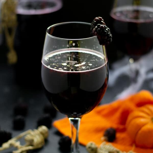 blackberry halloween sangria in a wine glass with fruit and pumpkins and skeletons on the table