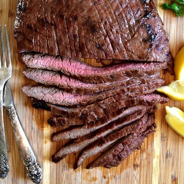 Overhead shot of grilled flank steak, half cut into strips showing off the pink meat inside