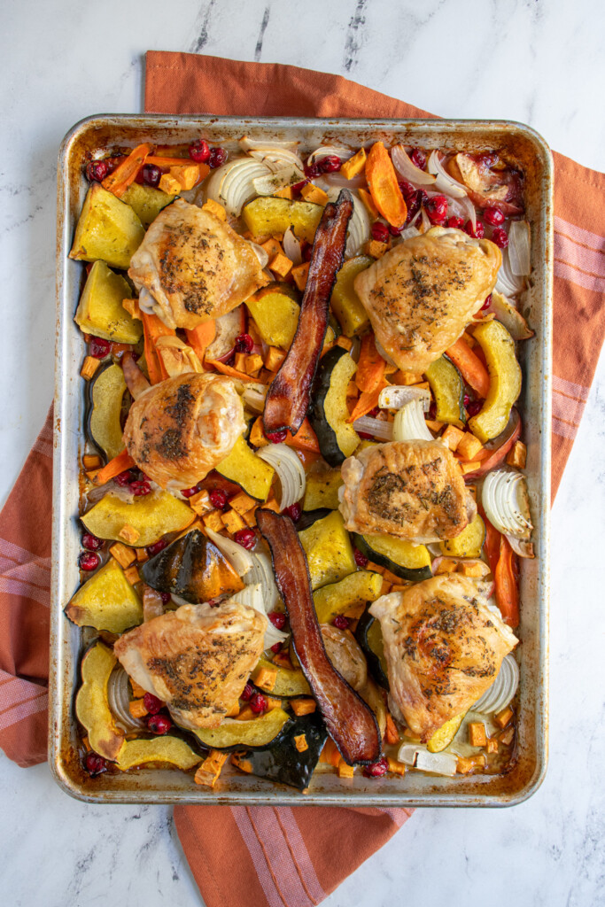 A sheet pan filled with seasonal fall veggies, chicken thighs, and bacon.