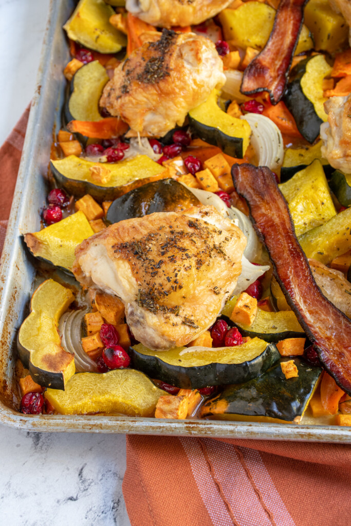Close up of a sheet pan filled with squash, cranberries, chicken, bacon, and more making it a one pan autumn chicken dinner.