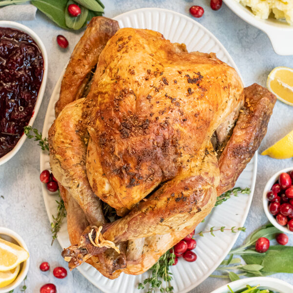 Overhead view of a full thanksgiving table with the roasted turkey in the center with crispy golden brown skin from dry brining on a large platter.