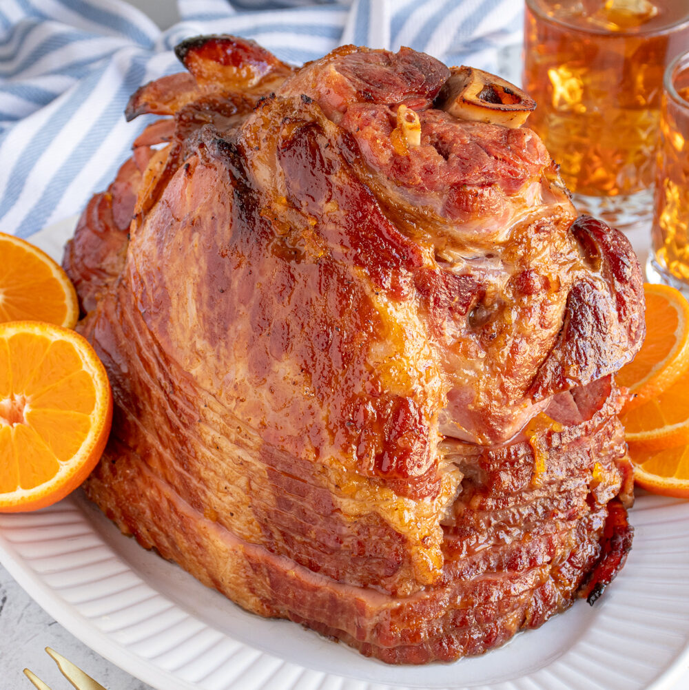 An Orange Bourbon Glazed Ham on a white platter garnished with orange slices.
