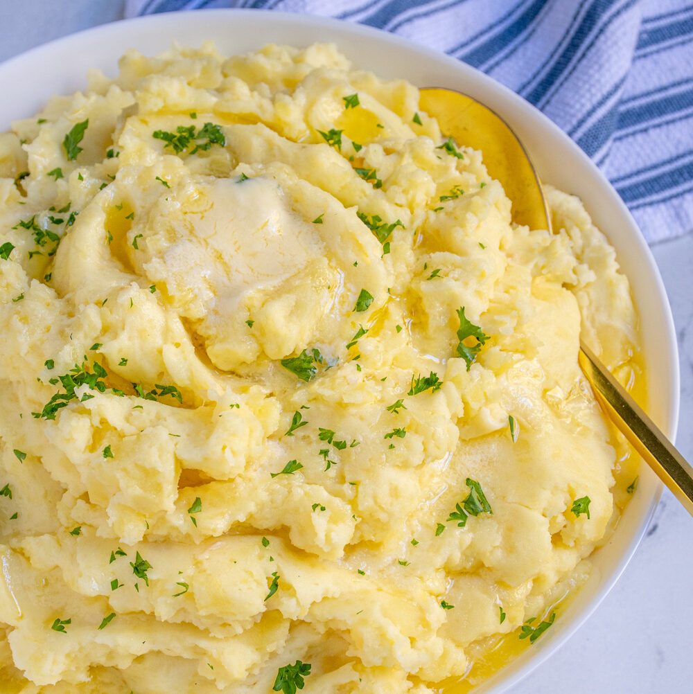 White bowl full of fluffy mashed potatoes dripping with melted butter and garnished with fresh parsley.