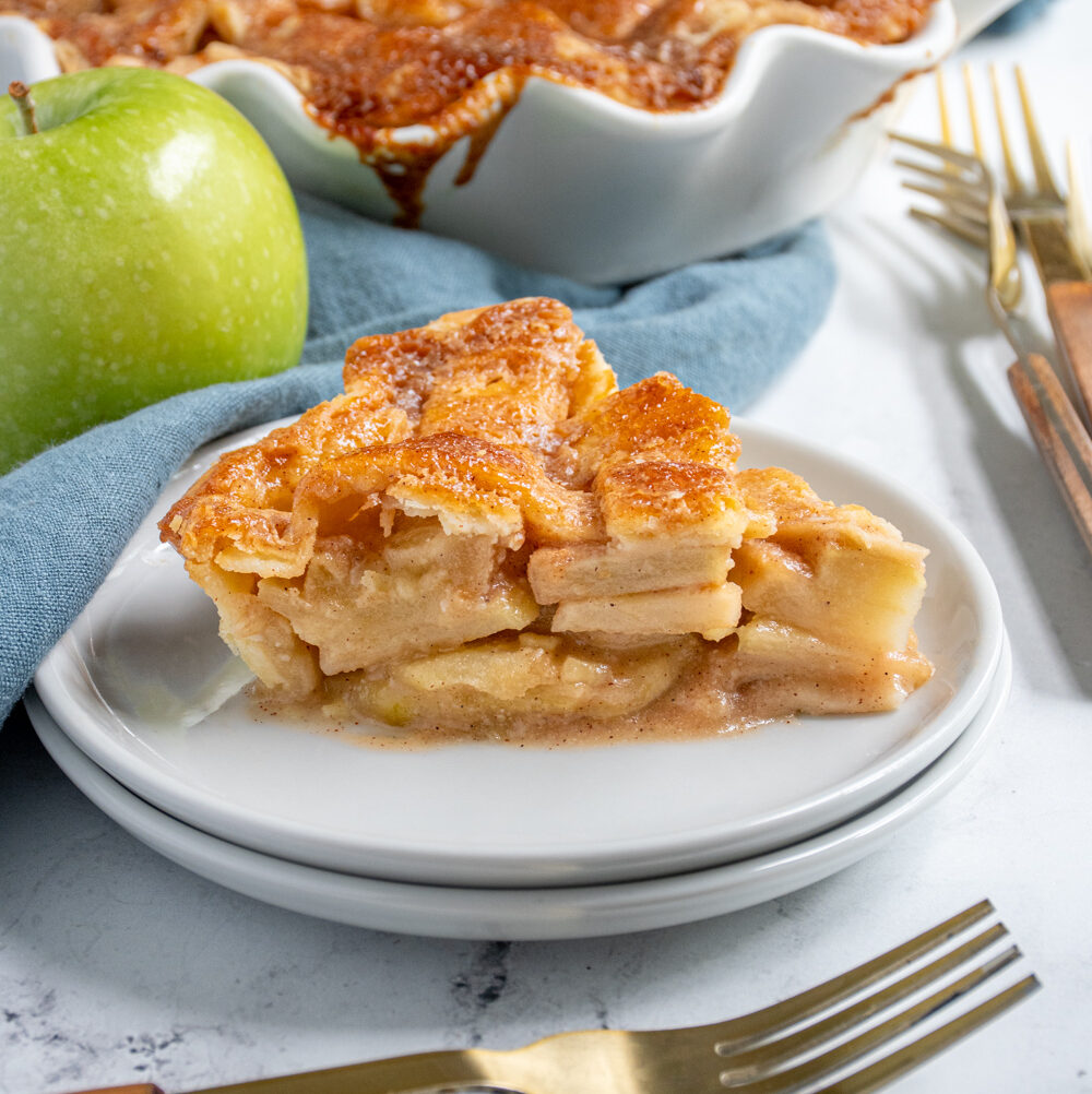 A slice of homemade apple pie on a plate showing of the apple inside and the lattice top.