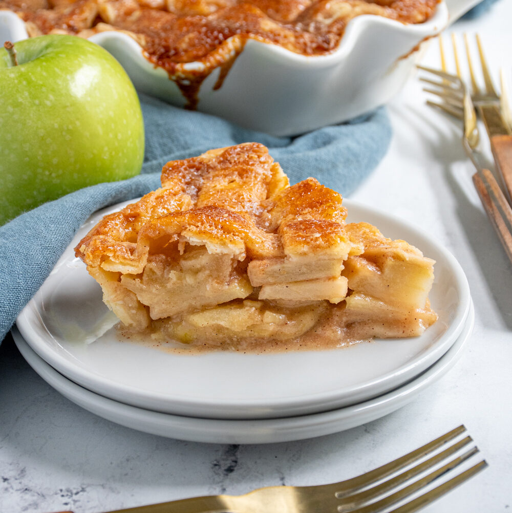 A slice of homemade apple pie on a plate showing of the apple inside and the lattice top.