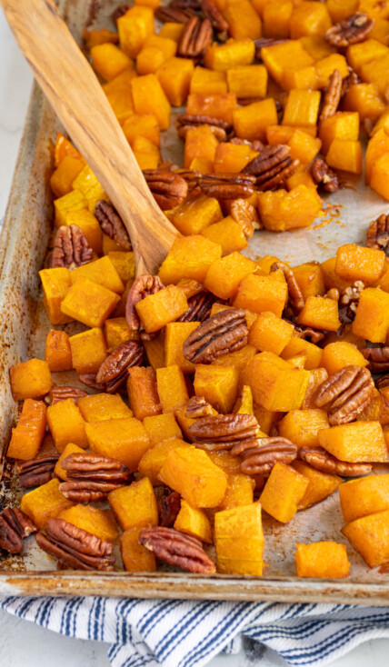 Sheet pan with roasted maple butternut squash with pecans, some scooped together with a wooden spatula.