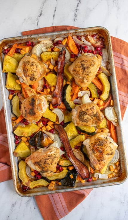 Overhead view of one pan autumn chicken dinner with squash, cranberries, onions, chicken, and bacon.