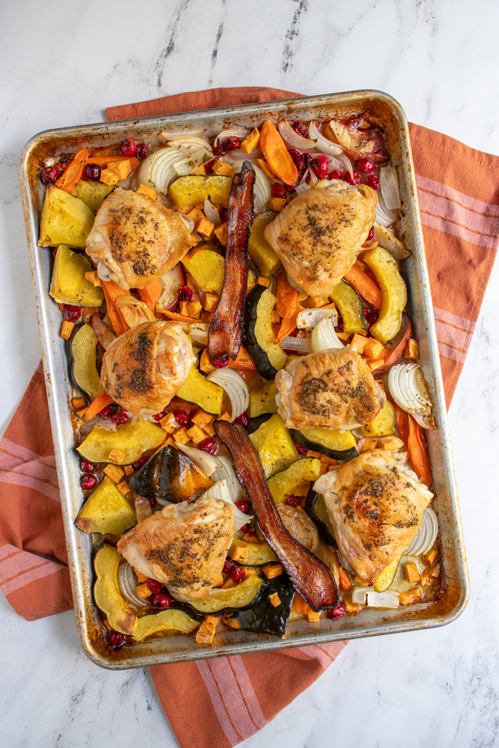 Overhead view of one pan autumn chicken dinner with squash, cranberries, onions, chicken, and bacon.