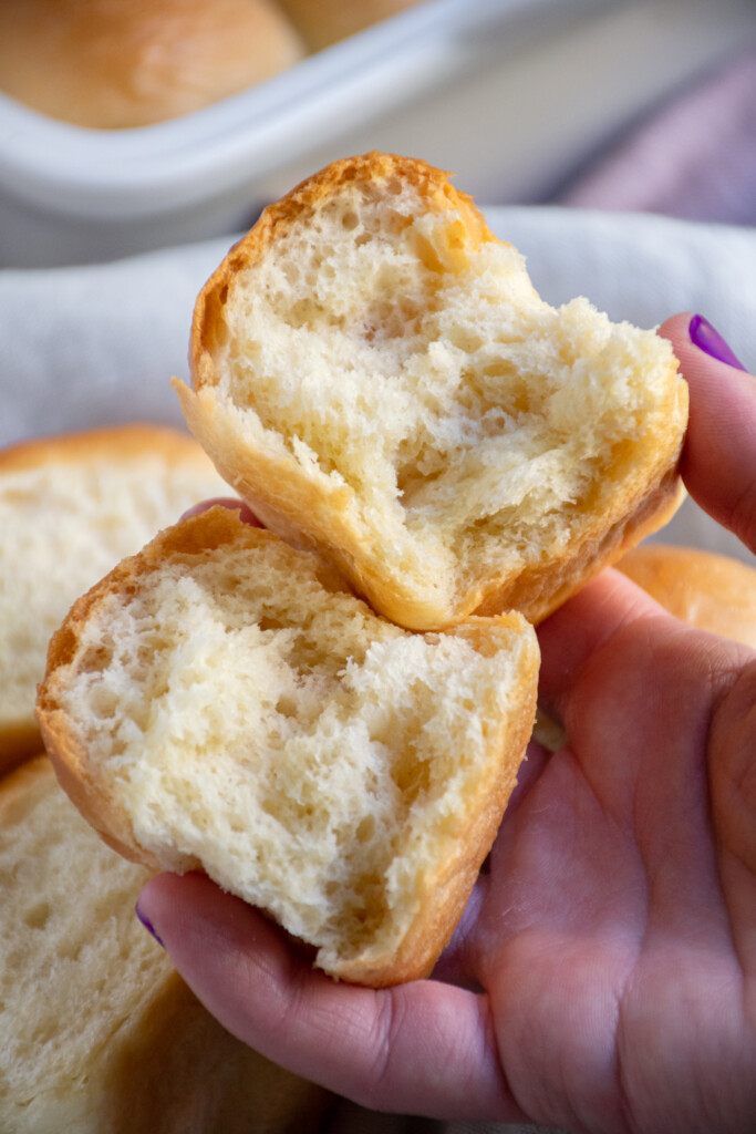 A soft homemade dinner roll broken into two pieces showing off the fluffy white insides.
