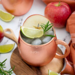 Pinterest pin with text overlay 'Apple Cider Moscow Mule', image of a copper mug full of apple cider mule garnished with apple, rosemary, and lime.