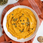 Pinterest pin with logo "The Schmidty Wife", image of a bowl filled with orange colored pumpkin hummus.