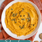 Pinterest pin with text "Pumpkin Hummus", image of a white bowl with orange pumpkin hummus garnished with olive oil and pumpkin seeds.