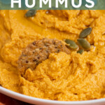 Pinterest pin with text "Pumpkin Hummus", image of a white bowl with orange pumpkin hummus garnished with olive oil and pumpkin seeds.