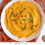 Pinterest pin with text "Pumpkin Hummus", image of a white bowl with orange pumpkin hummus garnished with olive oil and pumpkin seeds.