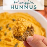 Pinterest pin with text "Pumpkin Hummus", image of a white bowl with orange pumpkin hummus garnished with olive oil and pumpkin seeds.
