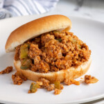 Pinterest Pin with text over lay 'Ground Turkey Sloppy Joes", image of a bun filled with sloppy joes on a plate.
