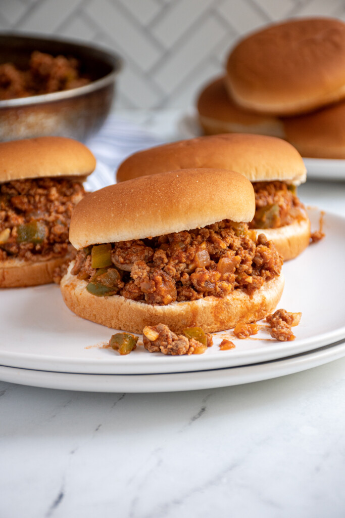 A plate with three buns filled with turkey sloppy joes spilling out.