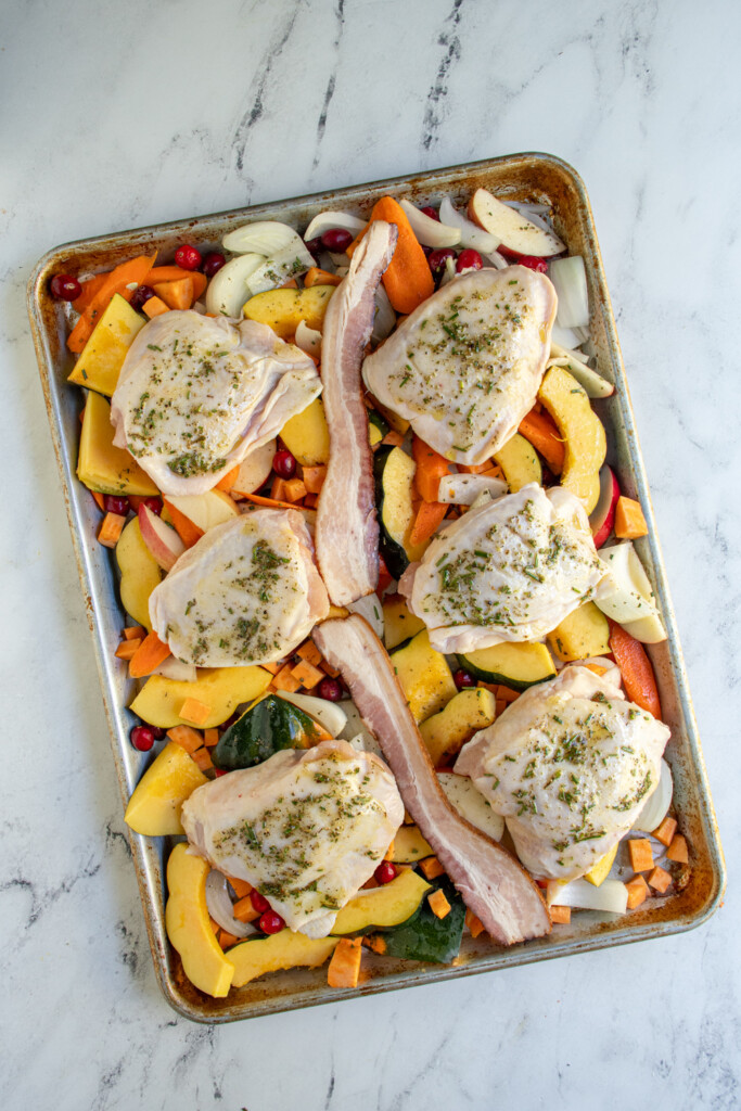 Overhead view of the raw sheet pan autumn dinner before going into the oven including the herbed oil on top of the chicken thighs.