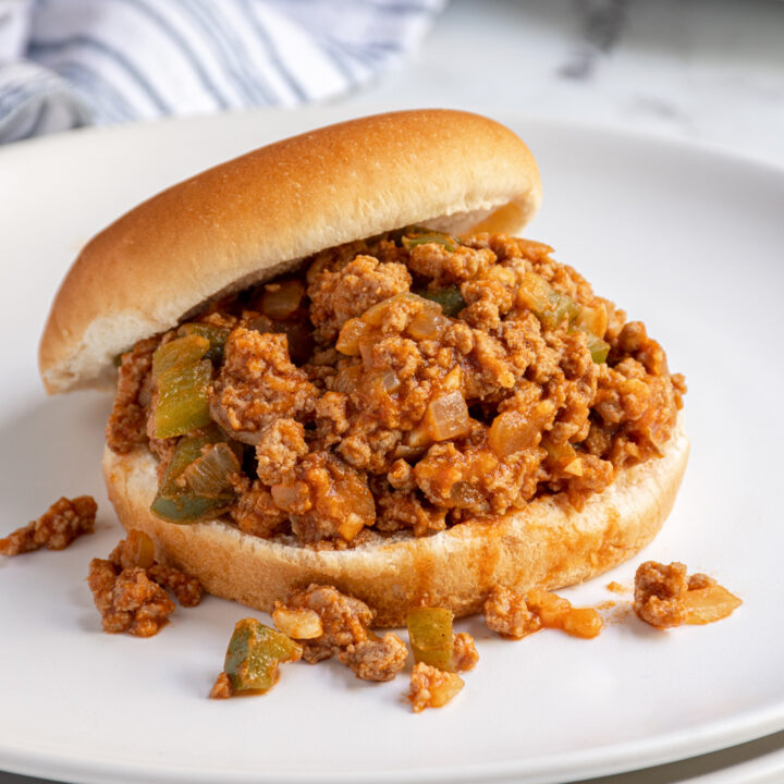 A bun on a white plate filled with ground turkey sloppy joes.